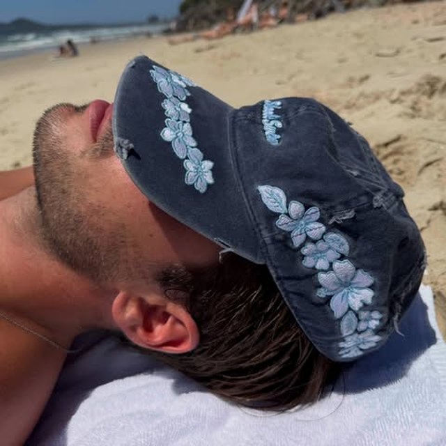 The Distressed Hibiscus Hat resting over a face on a beach towel in the sun